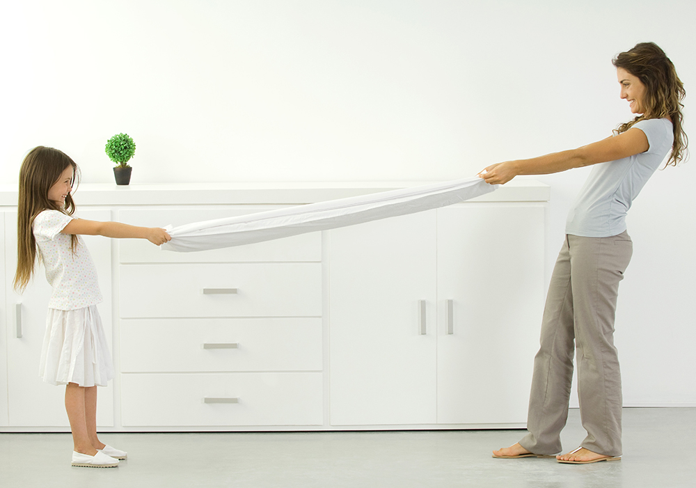 Mother and daughter folding a fitted sheet together